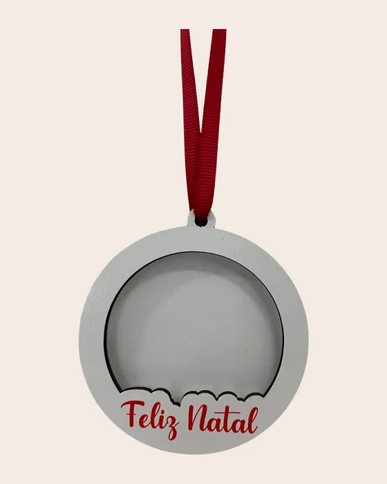 Bola de Natal em madeira branca com uma abertura redonda para uma fotografia e as palavras «Feliz Natal» em relevo vermelho, pendurada por fita vermelha.